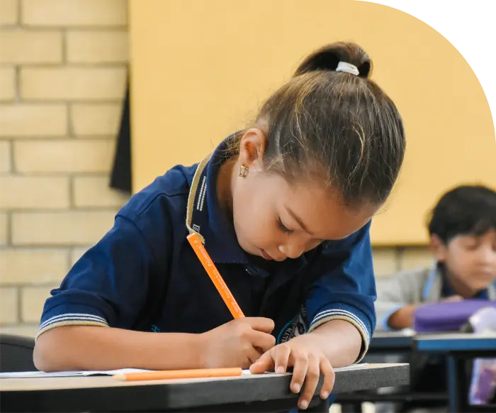 Foto de una niña de 5 años en clase de ingles con Morphy, sostiene un lápiz y escribe en un cuaderno. 