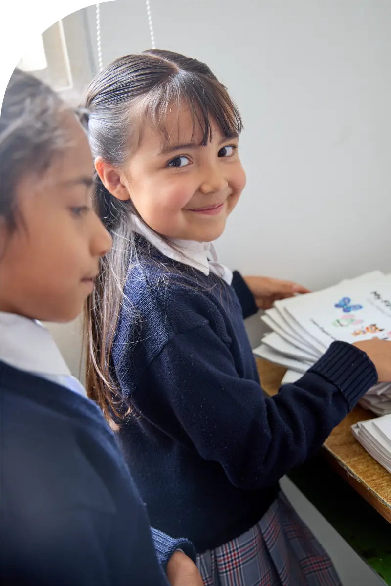 foto de dos niñas de 7 años. Una niña mira a la cámara y sonríe en sus manos tienes las cartillas Moprhy. Hace parte de la pagina evidencia