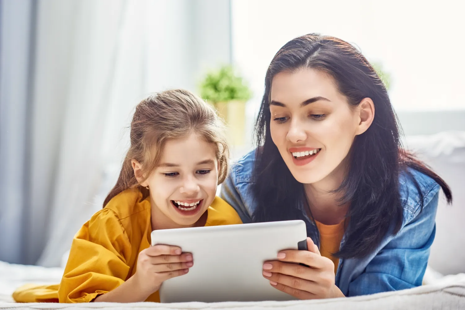 Mamá acompañando a su hija, que aprende en una tablet; las dos se ríen