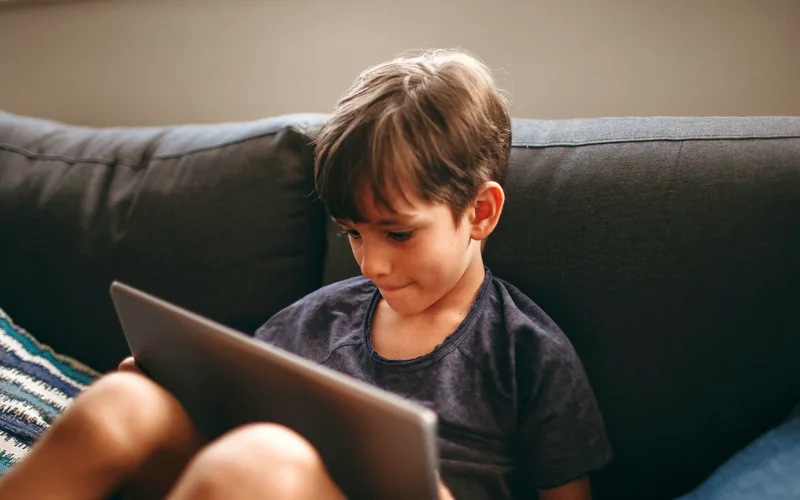 Niño concentrado en una tablet, sentado en el sofá de su casa