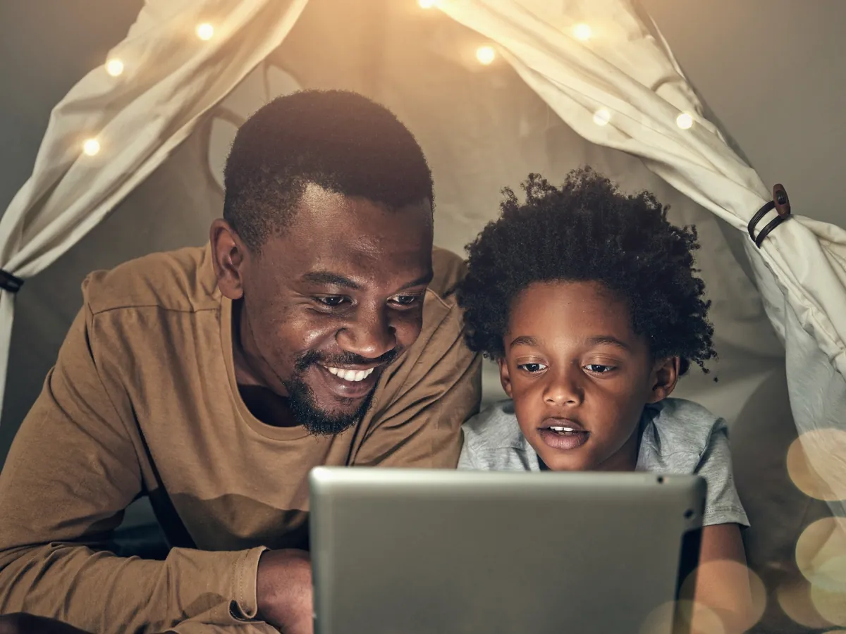 Papá e hijo sonriendo frente a una tablet, en su rato del día para aprender inglés en casa